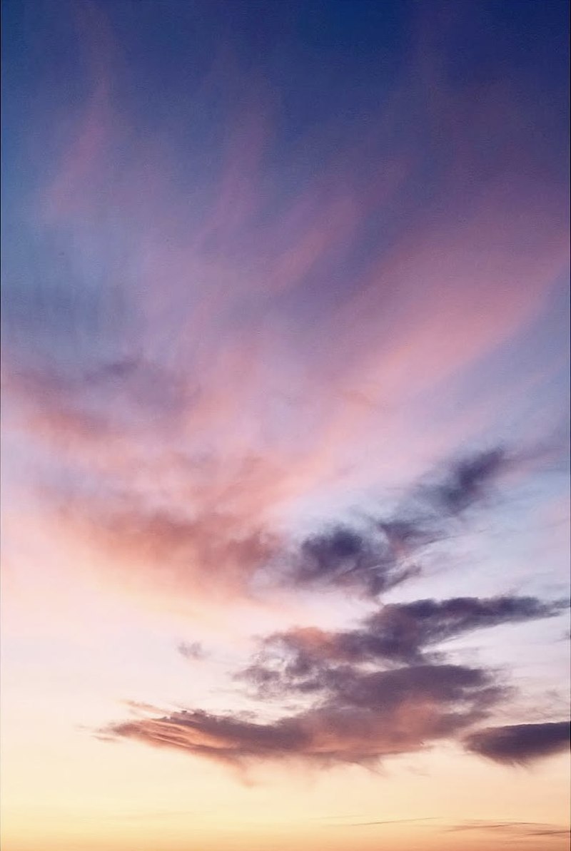 A summer sky at dusk over Chalkwell Beach in Southend-on-Sea. Deep blue at the top, wispy pink and peach clouds through the middle, and a warm cream horizon at the bottom, with dark cloud shapes catching the last warm light.